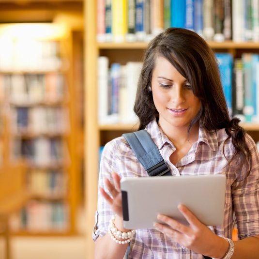 Cute young student using a tablet computer in a library